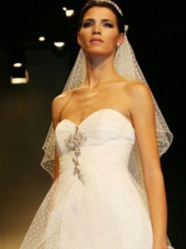 Una modelo presenta un vestido de novia blanco con un velo largo y elegante, destacando la belleza y la sofisticación de la prenda.