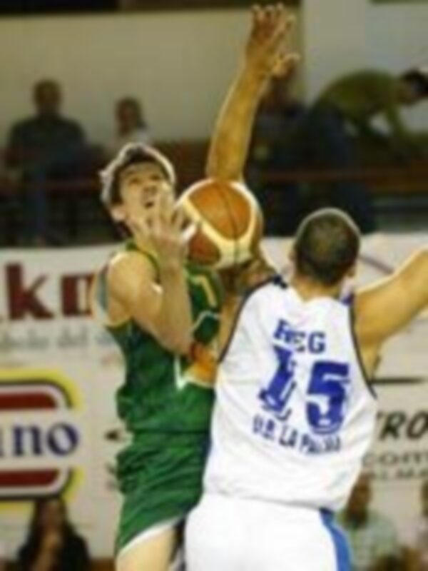 Jugadores en acción durante un partido de baloncesto, uno intenta rebotear mientras el otro intenta bloquear.