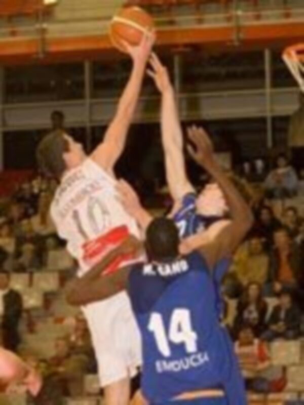 Juego de baloncesto en un estadio lleno, con un jugador en acción levantando el balón.