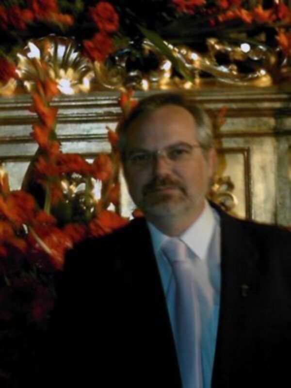 Hombre con traje y corbata en un entorno decorado con flores y ornamentos dorados.