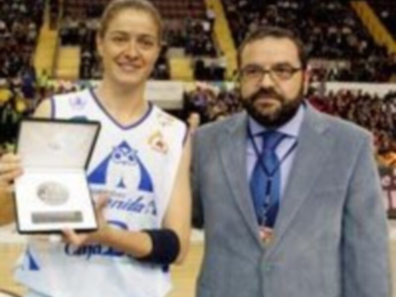 Jugadora de baloncesto recibe un premio de manos de un hombre en un entorno deportivo.