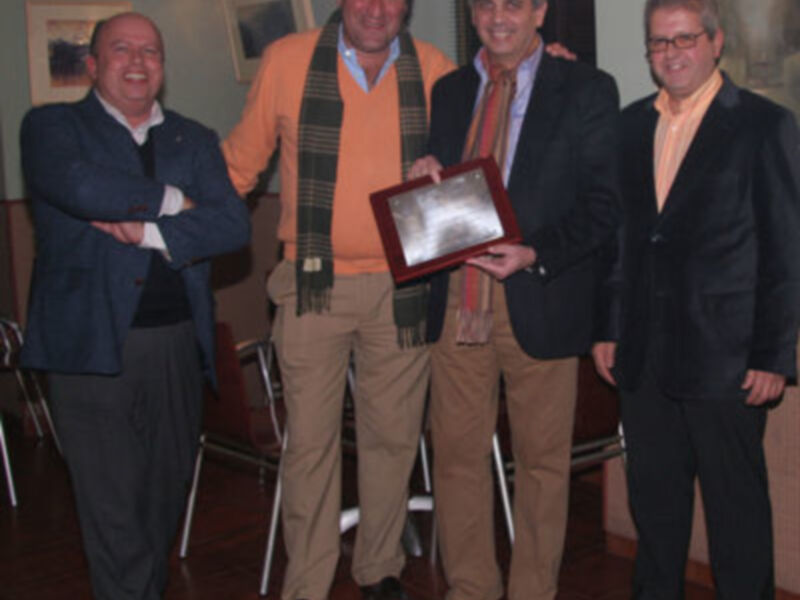 Cuatro hombres posan juntos, uno sostiene un trofeo, en una reunión formal.