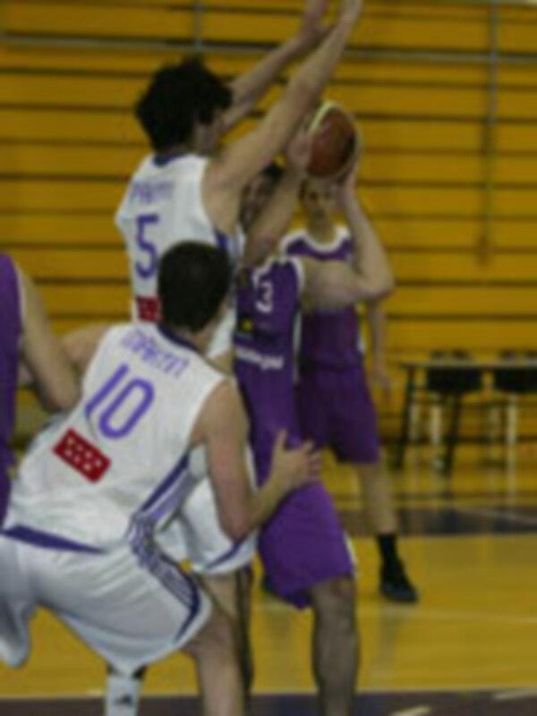 Un jugador de baloncesto en acción, con una camiseta azul y una camiseta púrpura en el fondo, durante un partido de baloncesto en una cancha de baloncesto.