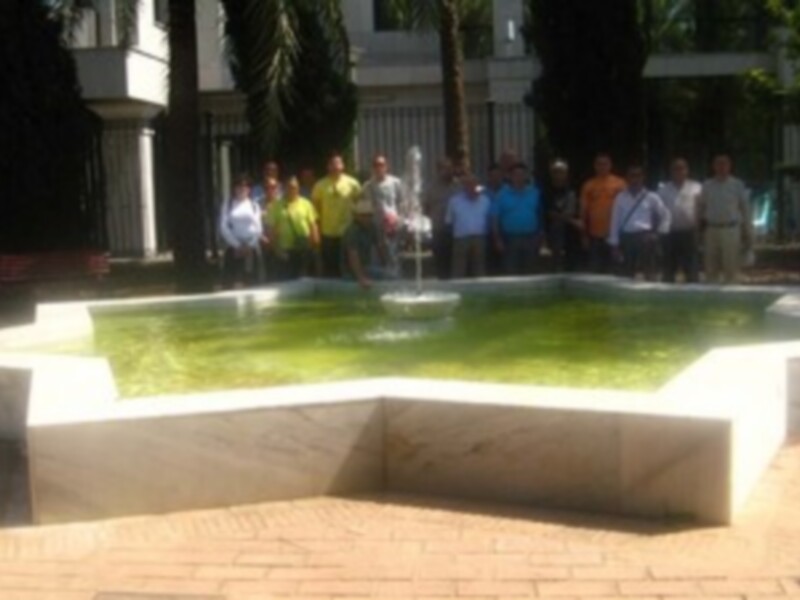 Gruppo di persone in piedi davanti a una fontana in un giardino con alberi e pavimentazione in pietra.