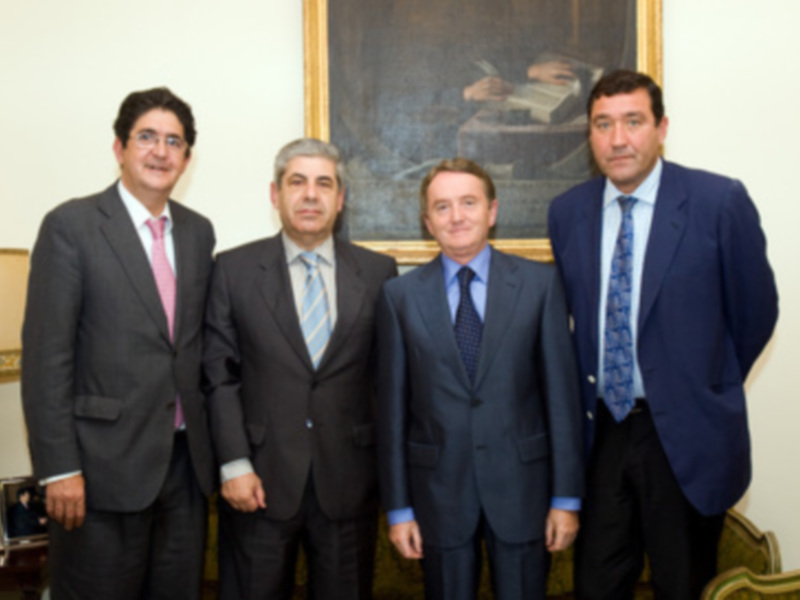 Cuatro hombres en trajes de negocios posando juntos en un entorno formal.