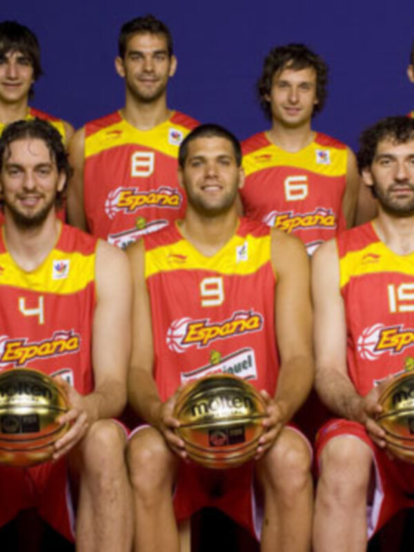 Equipo nacional español de baloncesto posando con sus camisetas rojas y amarillas, sosteniendo balones dorados.