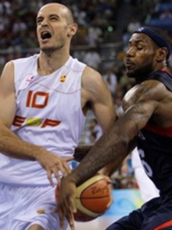 Dos jugadores de baloncesto en acción durante un partido, uno con una camiseta blanca y otro con una camiseta azul y roja, ambos en una postura de juego intensa.