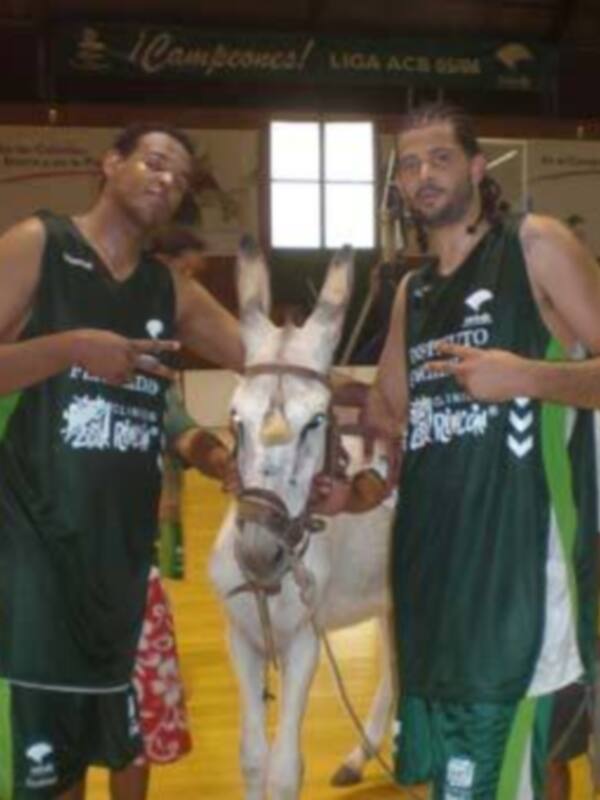Jugadores de baloncesto posan con un burro en un campo de baloncesto.