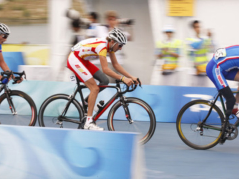 Ciclistas en acción durante una competición de ciclismo indoor, con un fondo azul y amarillo.