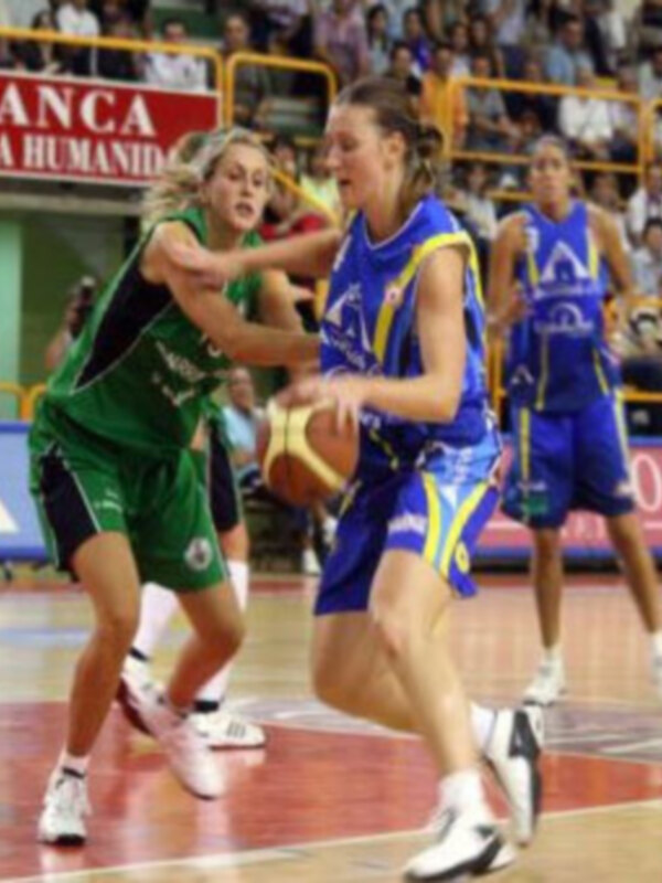 Jugadoras de baloncesto en acción durante un partido, una en verde y otra en azul, en un estadio lleno de espectadores.