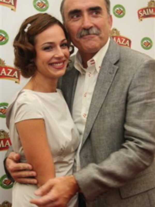 Una pareja sonríe juntos en un evento, rodeados de logotipos de cerveza.