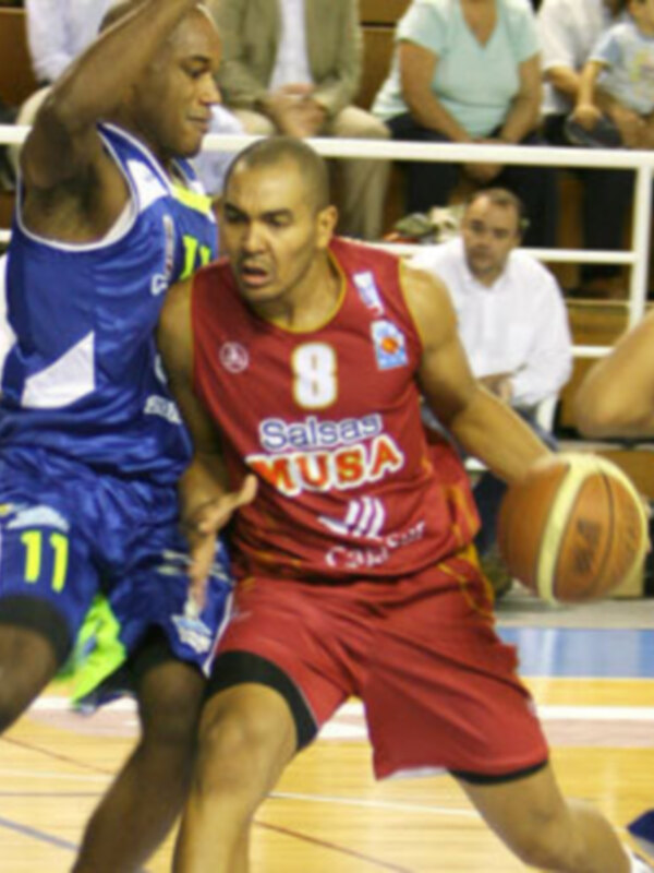 Jugador en rojo driblando durante un partido de baloncesto en una cancha deportiva.