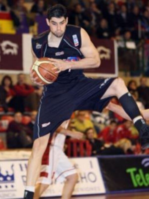 Un jugador de baloncesto en acción, con el balón en la mano, durante un partido de baloncesto en un estadio lleno de espectadores.