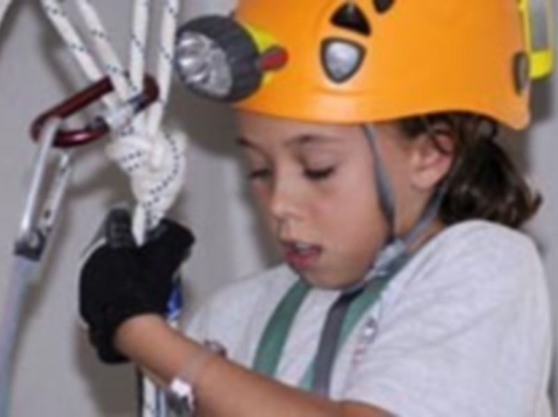 Un niño con casco de seguridad y guantes, trabajando en una cuerda.