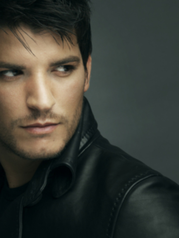 Retrato de hombre con chaqueta de cuero, expresión seria y fondo oscuro.