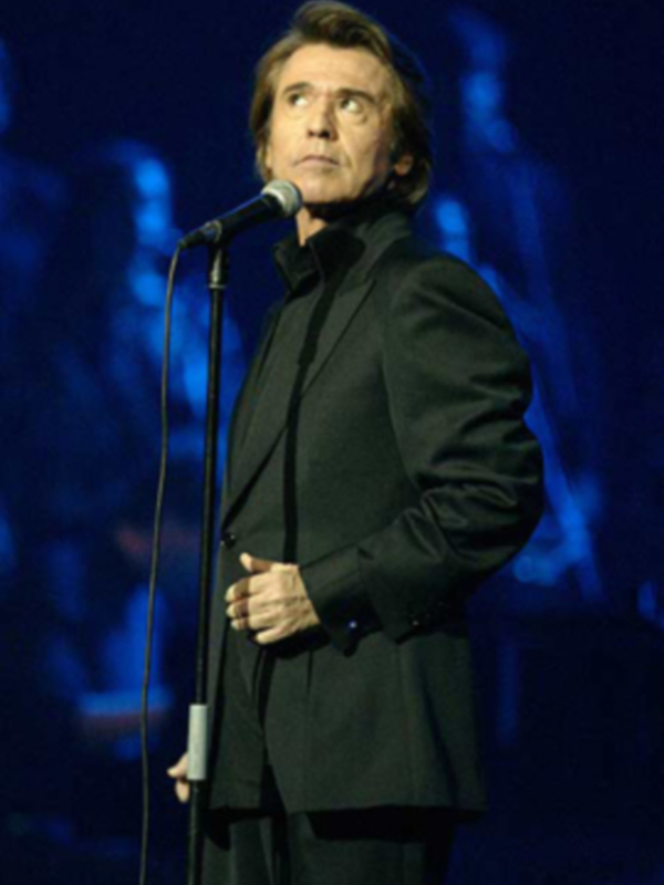 Cantante en escenario con micrófono, vestido con traje negro, iluminado con luz azul.