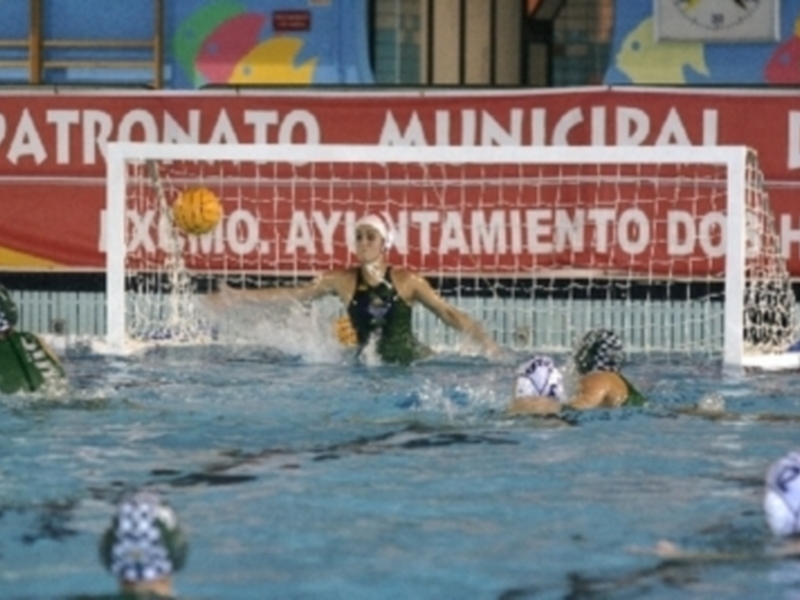 Juego de waterpolo en una piscina con un marcador de agua municipal en el fondo.
