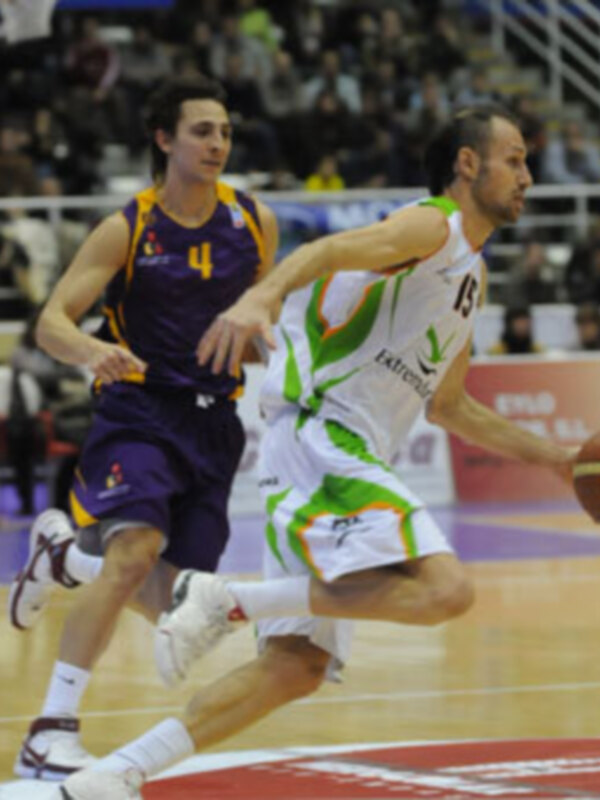 Jugador en acción durante un partido de baloncesto, driblando el balón con un rival en persecución.