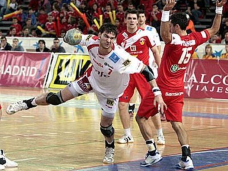 Jugador de balonmano en acción durante un partido, luchando por el balón en el centro del campo.