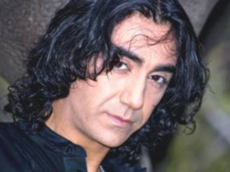 El pié de foto es un retrato de una persona con cabello largo y ondulado, vistiendo una camisa blanca. La imagen es de alta calidad, enfocada en el rostro y la parte superior del torso.