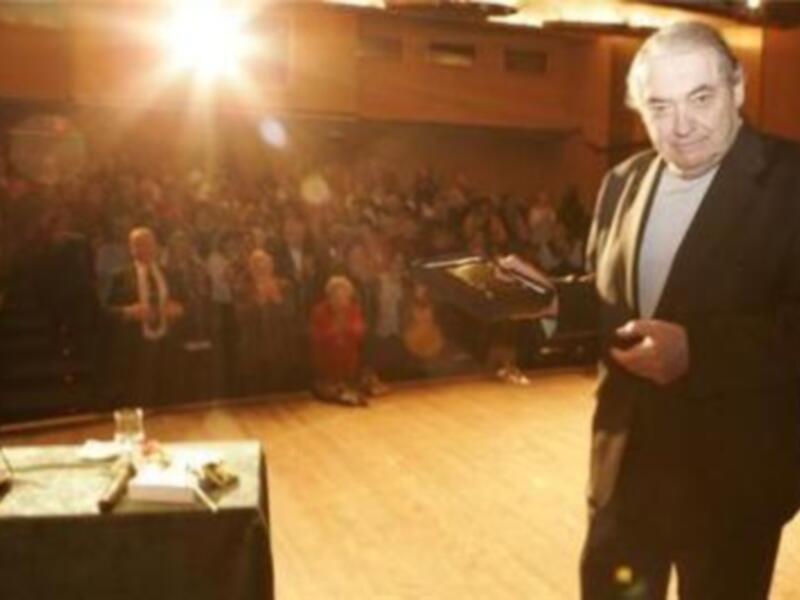 Un hombre en un escenario frente a una audiencia, posiblemente dando una conferencia o presentación.