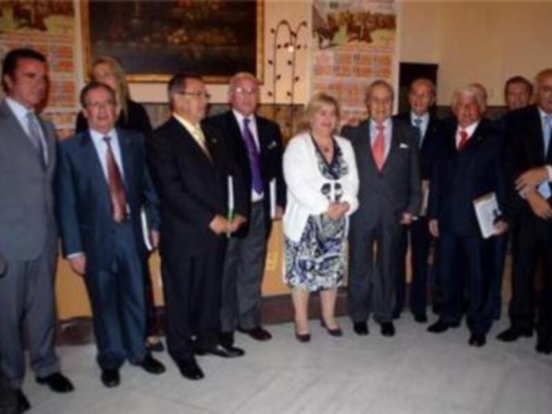 Un grupo de personas en trajes y vestidos formales posa para una foto en un interior decorado con detalles históricos.