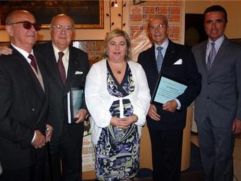 Conmemoración de un evento con reconocimiento, cuatro personas en trajes formales en un ambiente formal.