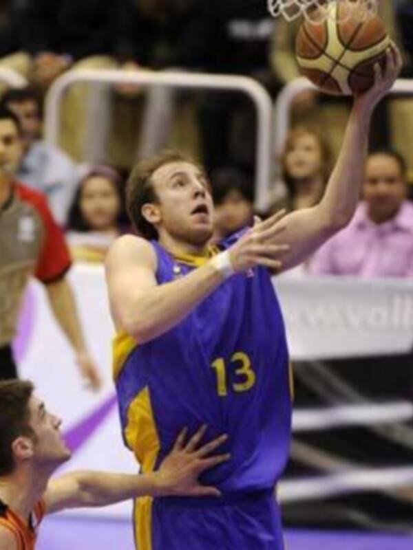 Un jugador de baloncesto en acción durante un partido, con el número 13 en su camiseta, intentando anotar un tiro libre mientras es defendido por un jugador del equipo contrario.