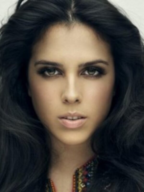 Una mujer con cabello largo y oscuro, posando con un atuendo casual y una joyería visible.