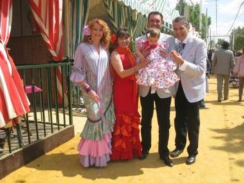 Familia celebrando en trajes típicos de feria, con un fondo de color amarillo y decoración festiva.