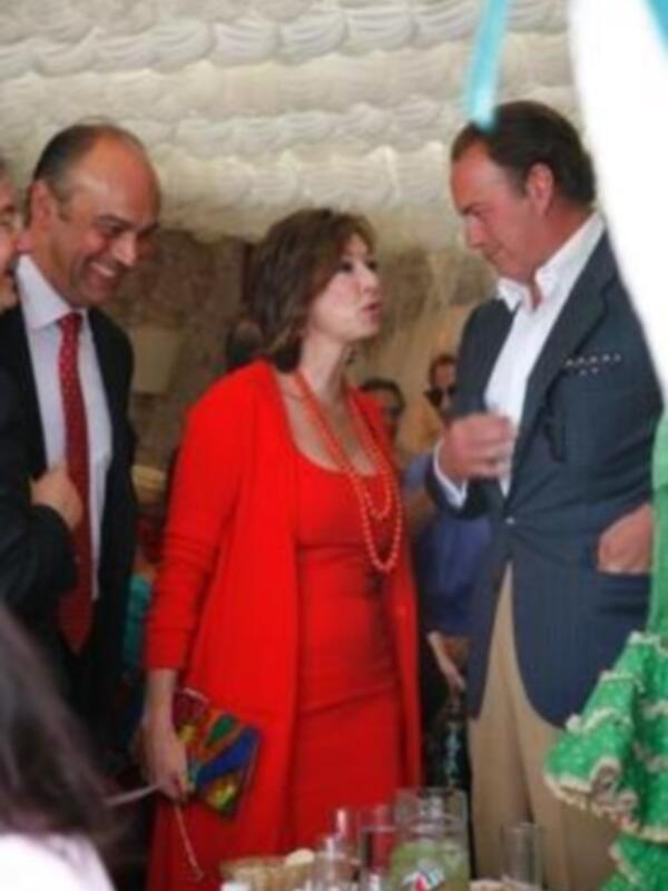 Una celebración festiva con personas vestidas formalmente, incluyendo una mujer en un vestido rojo brillante. La atmósfera parece ser una reunión social o una fiesta formal.