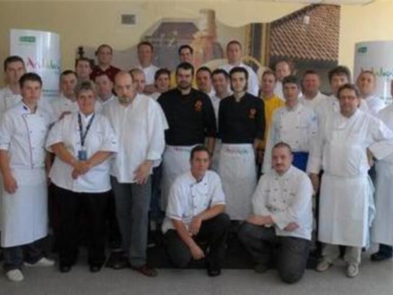Grupo de personas vestidas con uniformes de cocina, posando para una foto en un entorno profesional.