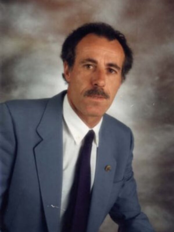 Retrato de hombre con traje azul y corbata, fondo degradado de tonos grises y marrones.