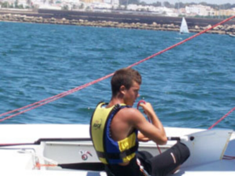 Un hombre en un traje de neón se prepara para una actividad acuática, posiblemente windsurfing o kitesurfing en un agua azul profundo.
