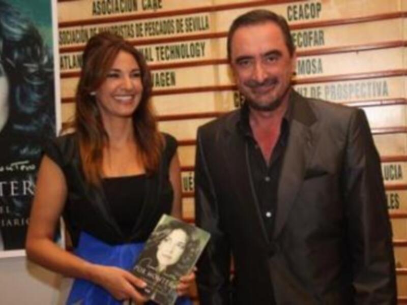 Persona con libro posa junto a cartel con retrato de mujer y texto en español.