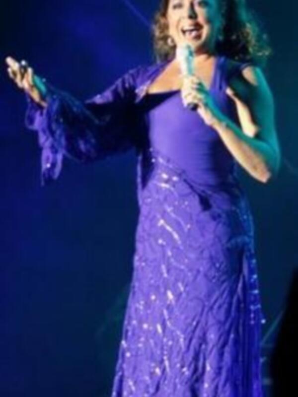 La cantante, vestida de púrpura con lentejuelas brillantes, canta en un escenario iluminado por luces azules.