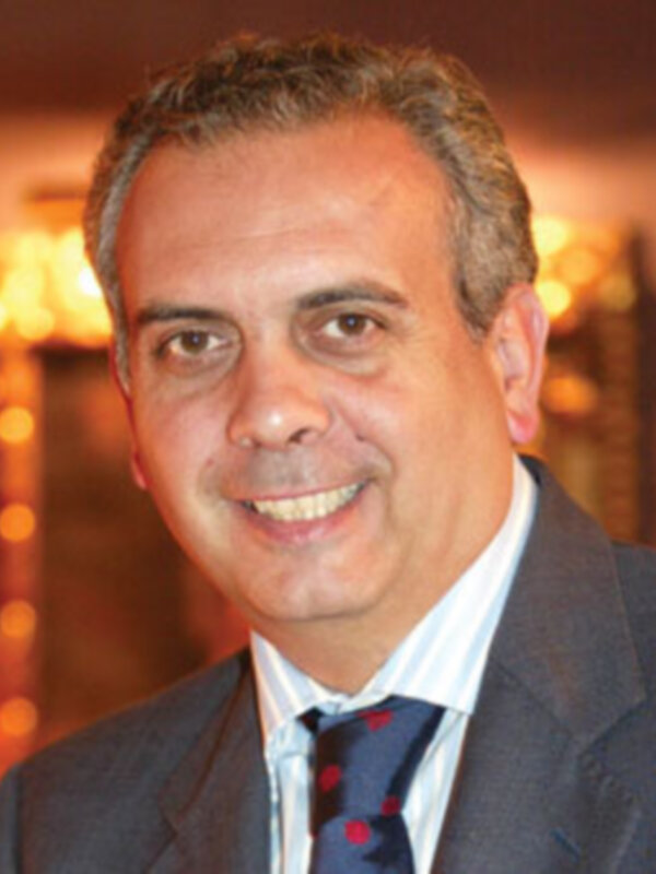 Retrato de hombre sonriente en traje y corbata, fondo con luces cálidas.