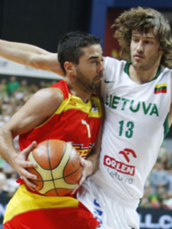 Dos jugadores de baloncesto, uno con camiseta roja y amarilla y otro con camiseta blanca y verde, en una acción de juego durante un partido de baloncesto.