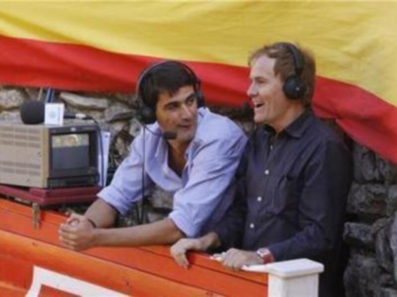 Dos personas con auriculares en un estudio de radio al aire, con un fondo de bandera española.