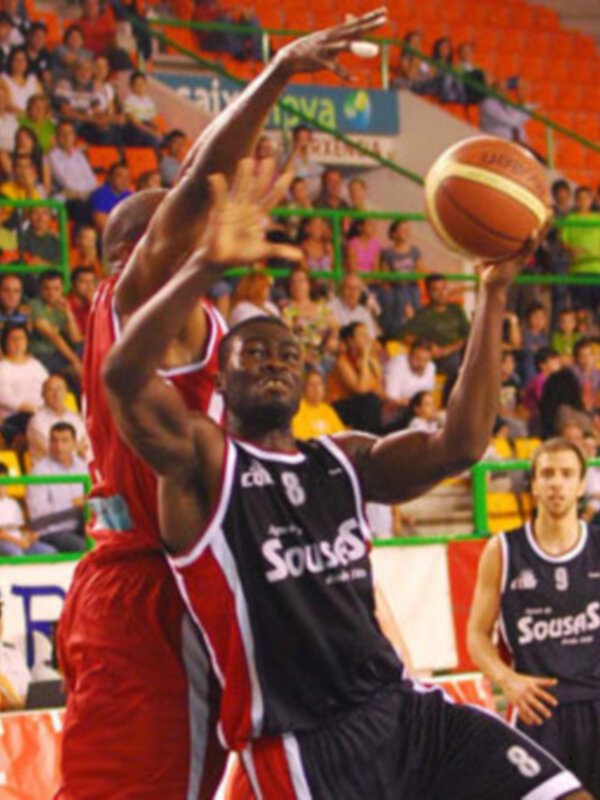 Jugadores de baloncesto en acción durante un partido en un estadio lleno de espectadores.