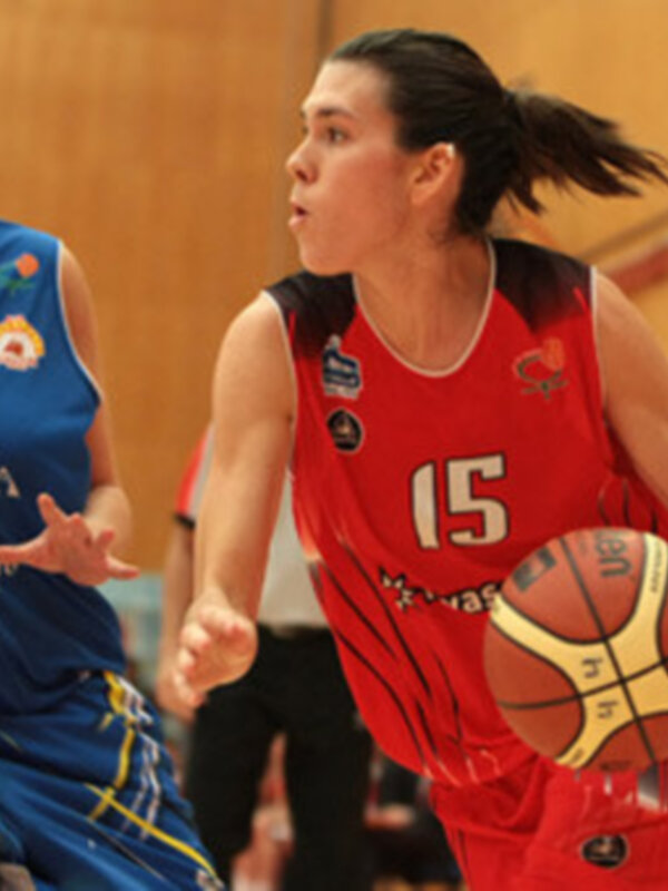 Jugadoras de baloncesto en acción durante un partido, una lleva la pelota y la otra la persigue.