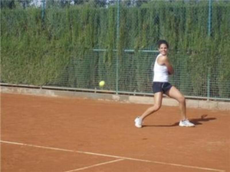 Una jugadora de tenis en acción, con una pelota en movimiento y un fondo de césped.