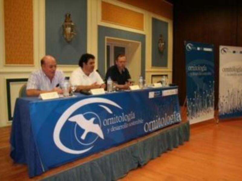 Conferencia de ornitología en un salón elegante con paneles informativos y participantes en una mesa redonda.