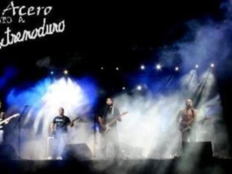 Una banda tocando en un escenario con luces y humo, titulada "De Arcero Tributo a Extremoduro".
