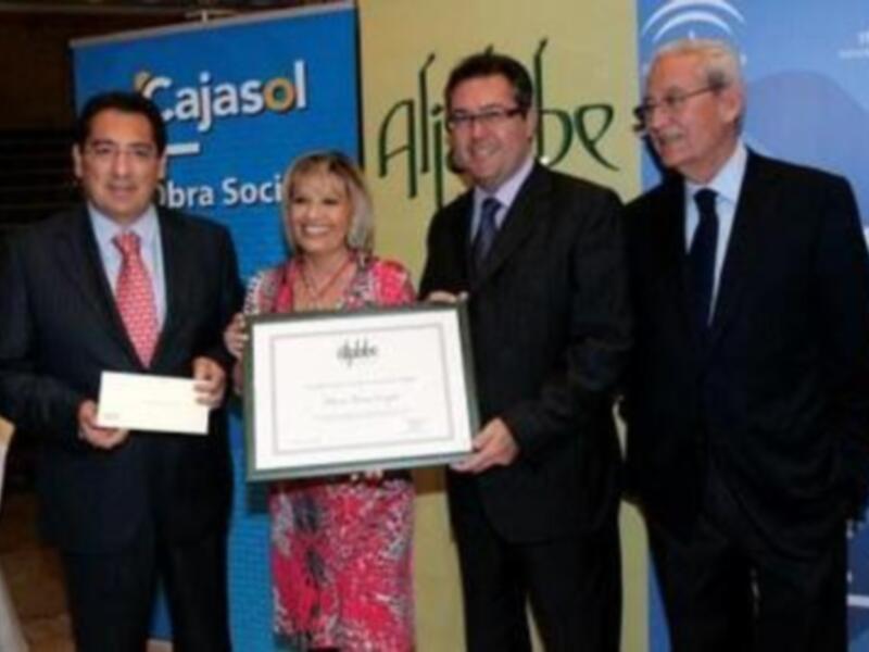 Una mujer sostiene un diploma mientras dos hombres la observan, con un fondo que incluye logotipos de Cajasol y Alibbe.