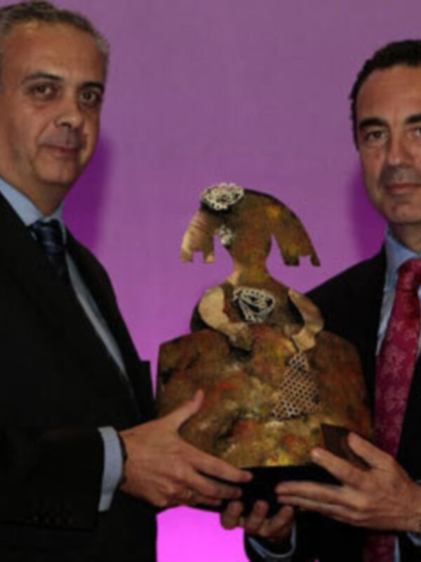 Dos hombres en trajes sostienen un objeto decorativo en un evento formal.