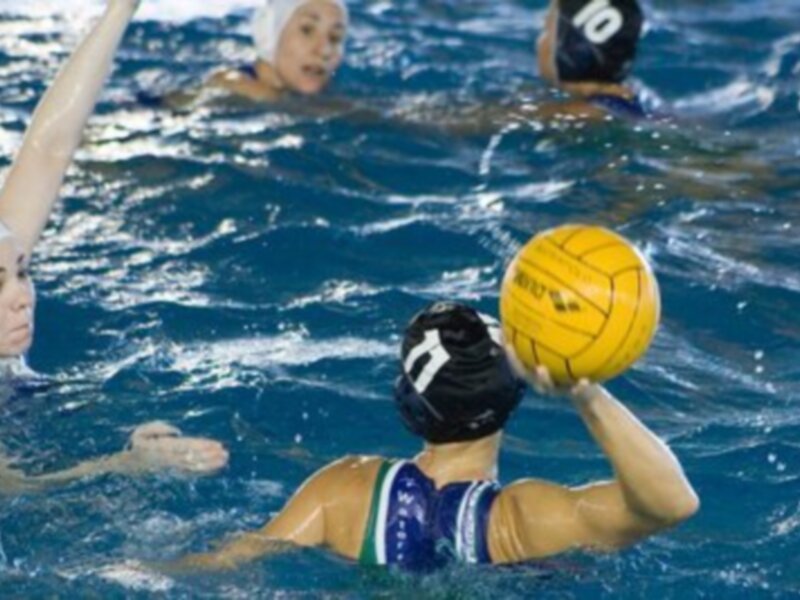 Jugadores de waterpolo en acción durante un juego, con un balón amarillo en el centro de la imagen.
