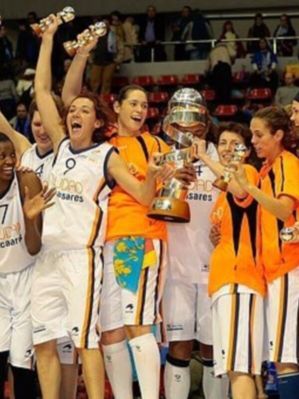 Equipo de baloncesto celebrando con trofeos en un escenario deportivo.