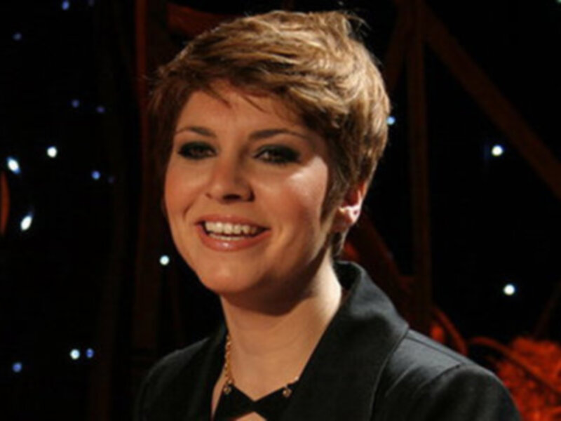 Una mujer con cabello corto y una sonrisa radiante, posando frente a un fondo con luces estrelladas.