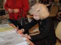 Una mujer mayor firmando un libro en una conferencia.